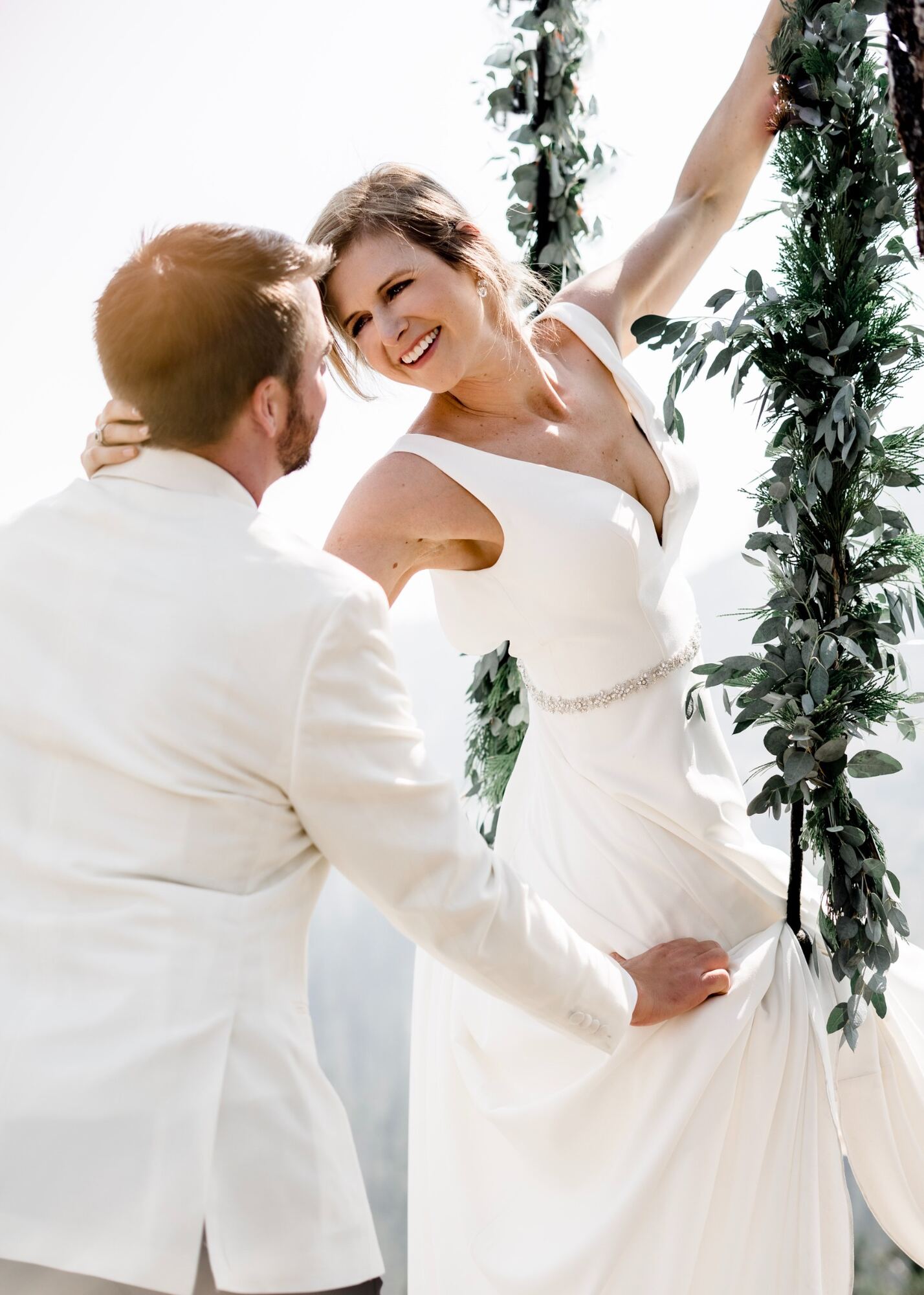 Bride smiling at her groom while sitting on a floral swing